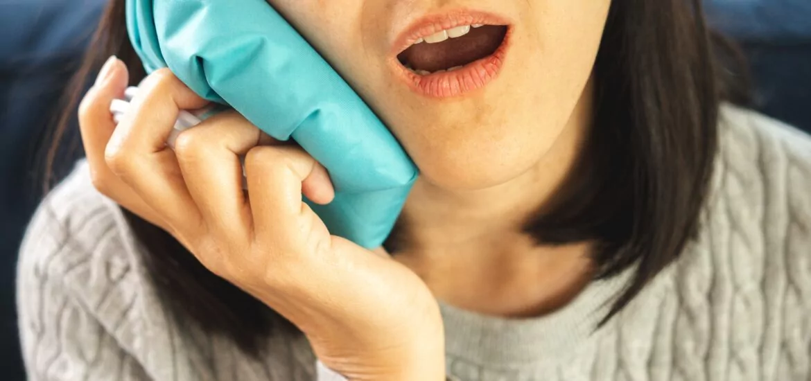 woman holding a blue ice pack on her tooth, severe tooth pain