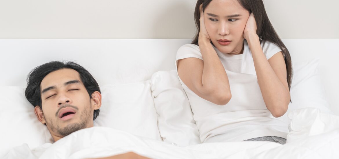 man snoring in a white bed disrupting his partners sleep
