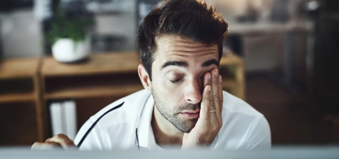 a fatigued man rubbing his eyes at his computer, sleep apnea signs