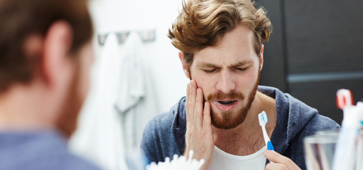 Man with sensitive teeth touching his jaw