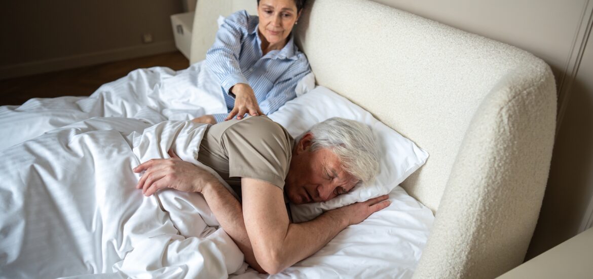 wife gently nudging her snoring husband in bed